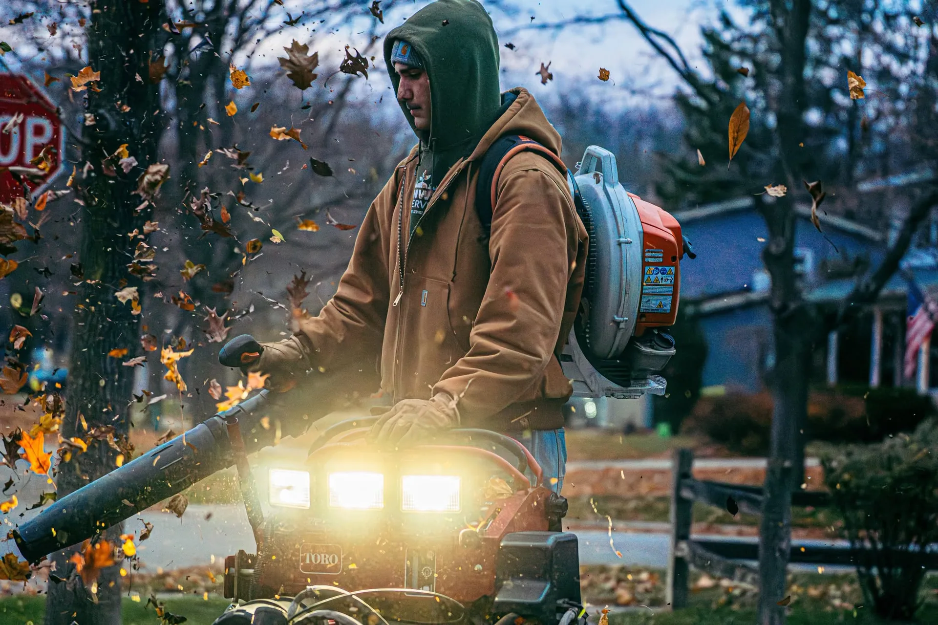 Greenworks crew member clearing leaves with a blower at dusk