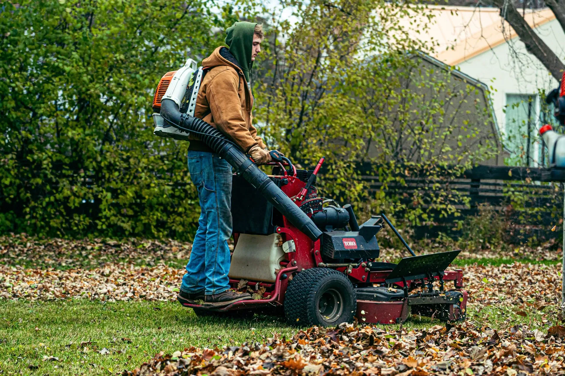 Greenworks crew using a blower and stand-on mower during leaf cleanup