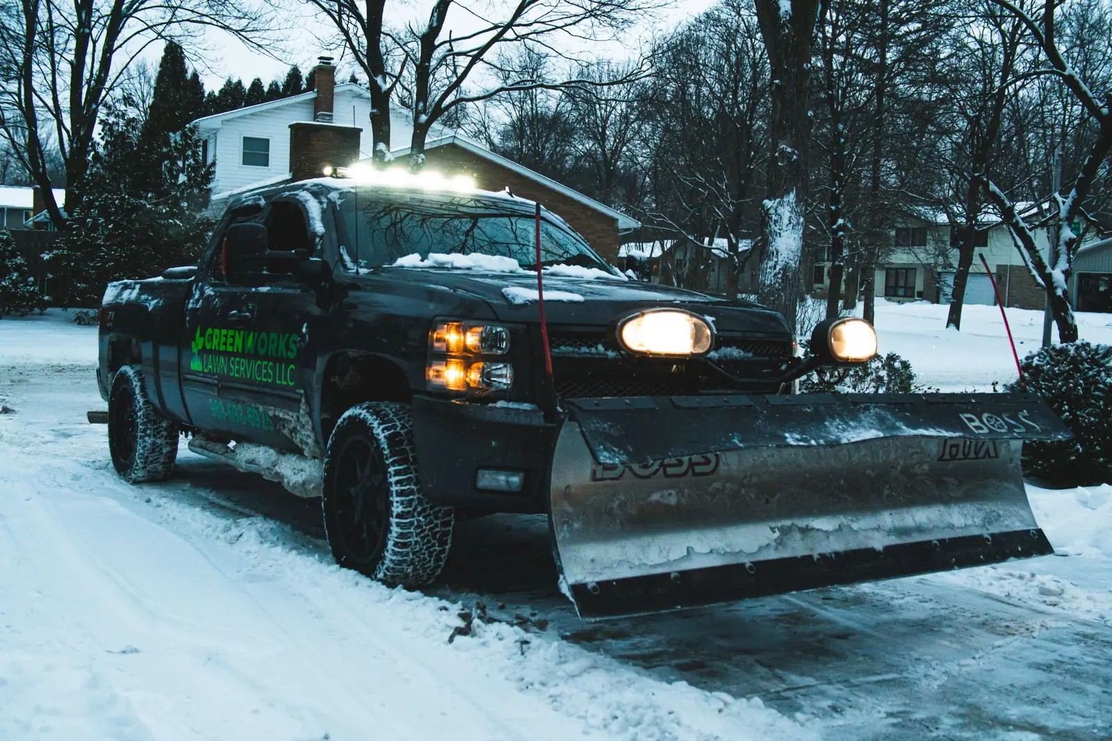 Greenworks plow truck with a BOSS blade clearing a snowy driveway